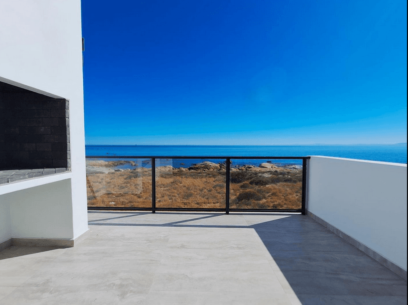 Modern white balcony with glass railing overlooking a rocky coastline and deep blue ocean.